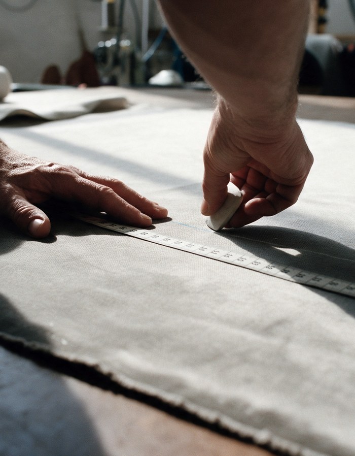 Les mains d'un tapissier mesurent un tissu et le marquent à la craie.